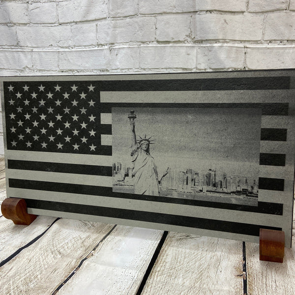 A scene of New York city skyline and the Statue of Liberty on the US flag. All laser engraved onto a piece of black slate.
