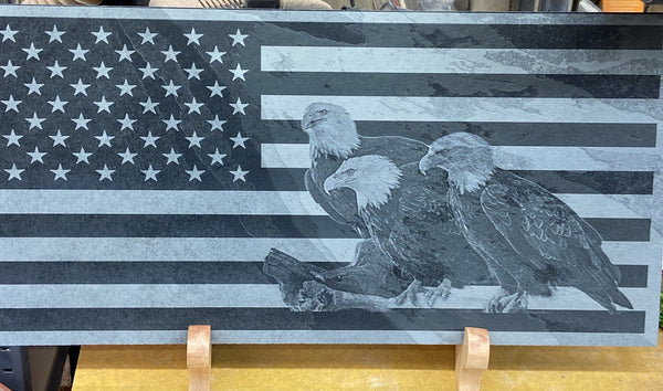 A beautiful laser engraved picture of three American Bald Eagles on the US flag. Done on a 24 inch by 12 inch piece of black slate, sitting on two maple wooden stands for displaying.