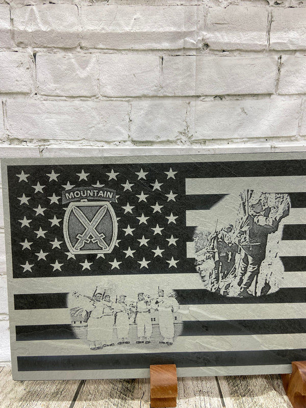A close up of the left side of the product showing the 10th Mountain patch in the US flag union section and two scenes on the stripes. One scene is of the 10th Mountain soldiers climbing the mountains in Riva Ridge, Italy and the other is of five 10th Mountain soldiers with their ski gear getting ready to patrol in Riva Ridge area in Italy. 