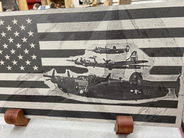 A laser engraving of the iconic B17, B24 and B25 on the US flag. Done on a 24 inch by 12 inch piece of black slate, displayed sitting on two mahogany wooden stands.