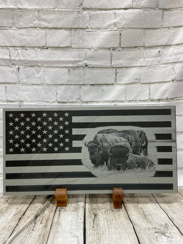 A herd of bison scene on the US flag laser engraved onto a piece of black slate.
